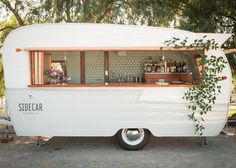 an old camper converted into a bar with plants growing out of the back window