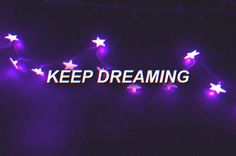 the words keep dreaming are lit up in purple and white stars on a black background