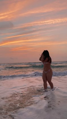 a woman standing on top of a sandy beach next to the ocean at sunset or dawn