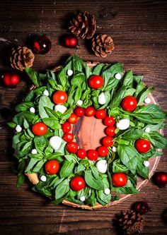 a wreath made out of tomatoes, basil leaves and pine cones on a wooden table