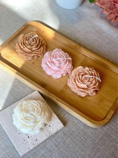 three pink and white flowers sitting on top of a wooden tray