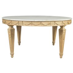 an oval marble top table with wooden legs and carved details on the base, against a white background