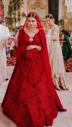 a woman in a red gown and veil walking down the aisle with other people behind her