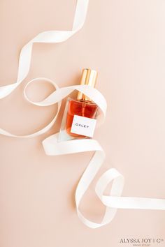 a bottle of perfume sitting on top of a white ribbon next to a pink wall