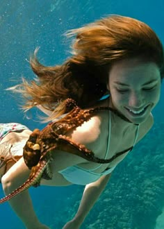 a woman is swimming under the water with her hair blowing in the wind and smiling