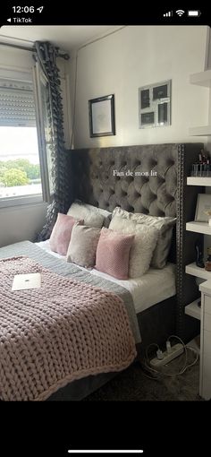 a bed with pink and gray pillows in a bedroom next to a window, framed pictures on the wall