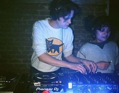 two young men are playing music on the dj's decks in front of a brick wall