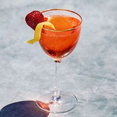 a glass filled with liquid and garnished with a strawberry on the rim next to a slice of lemon