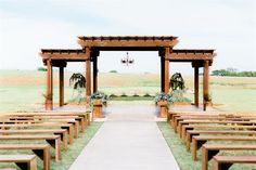 an outdoor wedding ceremony setup with wooden benches and flower arrangements on the aisle, in front of a grassy field