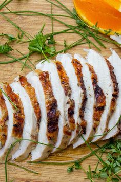 slices of sliced chicken sitting on top of a wooden cutting board next to an orange