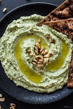 hummus and pita chips on a black plate with pesto sauce in the middle