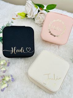 three personalized jewelry cases sitting on top of a white blanket next to some flowers