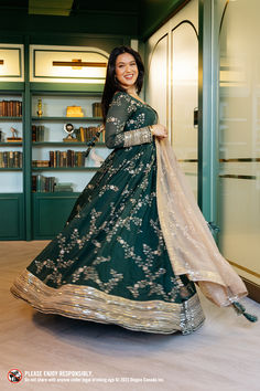 a woman in a green and gold dress posing for the camera with bookshelves behind her