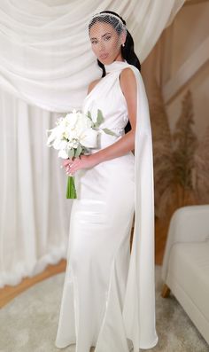 a woman in a white dress holding a bouquet and wearing a long veil over her head