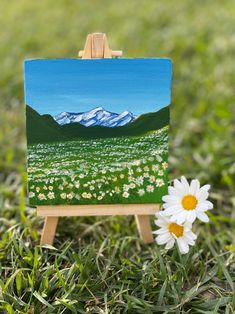 a small easel with a painting on it and a flower in the foreground