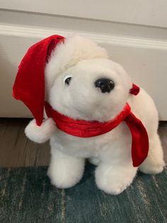 a white teddy bear with a red scarf around its neck sitting on the floor next to a door