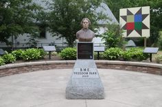 a statue of a person in front of a building with flags and trees behind it