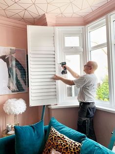 a man is working on the shutters of a window in his living room with pink walls