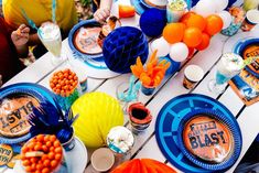 a table set with plates and decorations for an orange, blue and white birthday party