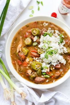 a white bowl filled with soup and rice on top of a table next to green onions