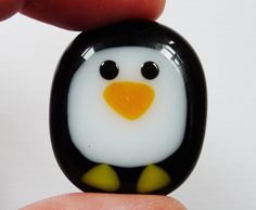 a small glass penguin sitting on top of a finger