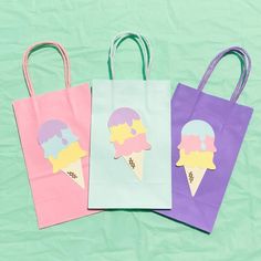 three bags with ice cream on them are sitting on a green surface, one is pink and the other is blue