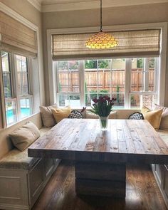 a wooden table sitting in the middle of a living room next to a large window