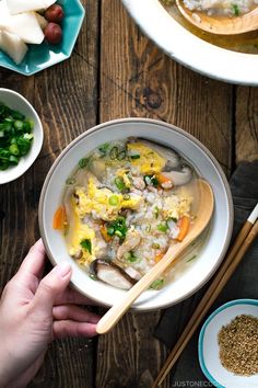 a person holding a wooden spoon over a bowl of rice and vegetables with chopsticks