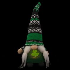 a green and black knitted gnome with a shamrock on it's head, standing in front of a black background