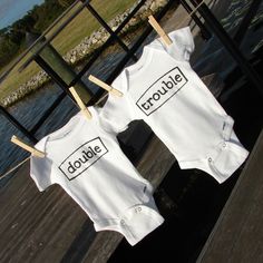 two baby onesuits that say double trouble hanging on a clothes line by the water