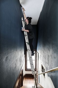 a woman climbing up the side of a stair case in a room with blue walls