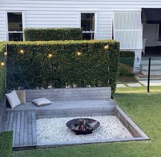 a fire pit in the middle of a lawn with lights on it and some bushes