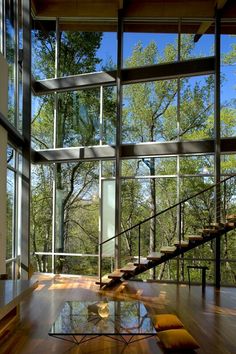 the inside of a modern house with wood floors and glass walls that look out onto trees