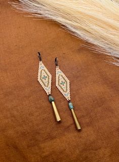 two beaded earrings sitting on top of a brown cloth next to a feathery object