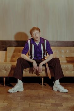 a young man sitting on top of a wooden chair in front of a brown couch