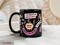 a black coffee mug with pink and purple designs on it, sitting on a bed