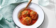 a white plate topped with meatballs covered in marinara sauce next to a glass of water