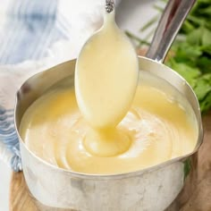 a ladle full of cheese sauce being poured into a pot with a wooden spoon