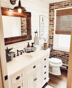 a bathroom with brick wall and white vanity, toilet and window in the corner area