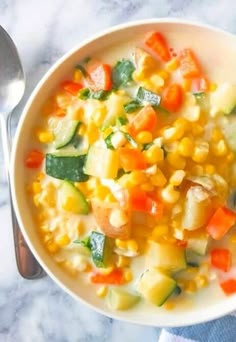 a white bowl filled with vegetable chowder next to a spoon