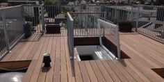 a wooden deck with metal railings and potted plants on the other side, in front of a cityscape