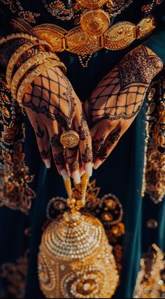 the hands of a woman with henna and jewelry on her arm, holding a golden vase