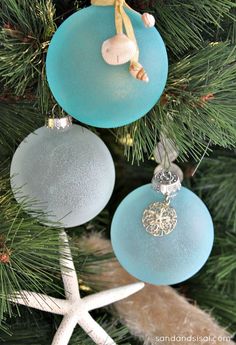 two glass ornaments hanging from a christmas tree with starfish and seashells on them