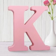 the letter k is painted pink next to a vase with flowers in it on a white table