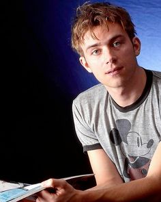 a young man sitting on a chair holding a book in his hand and looking at the camera