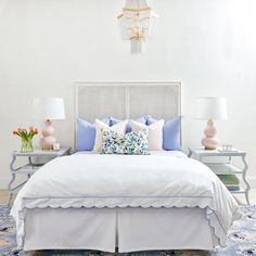 a white bed with blue and pink pillows in a bedroom next to two nightstands