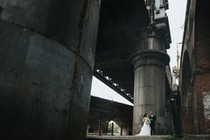 a bride and groom standing under an old bridge