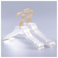 three clear acrylic clothes hangers with gold colored handles