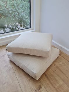 two pillows sitting on top of each other in front of a window with trees outside