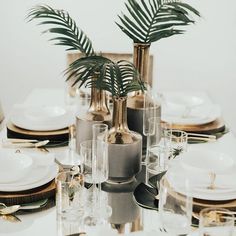 the table is set with gold and white plates, silverware, palm trees, and candlesticks